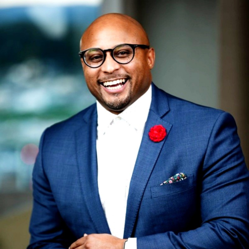 Oyango Snell smiling in a blue suit and glasses.
